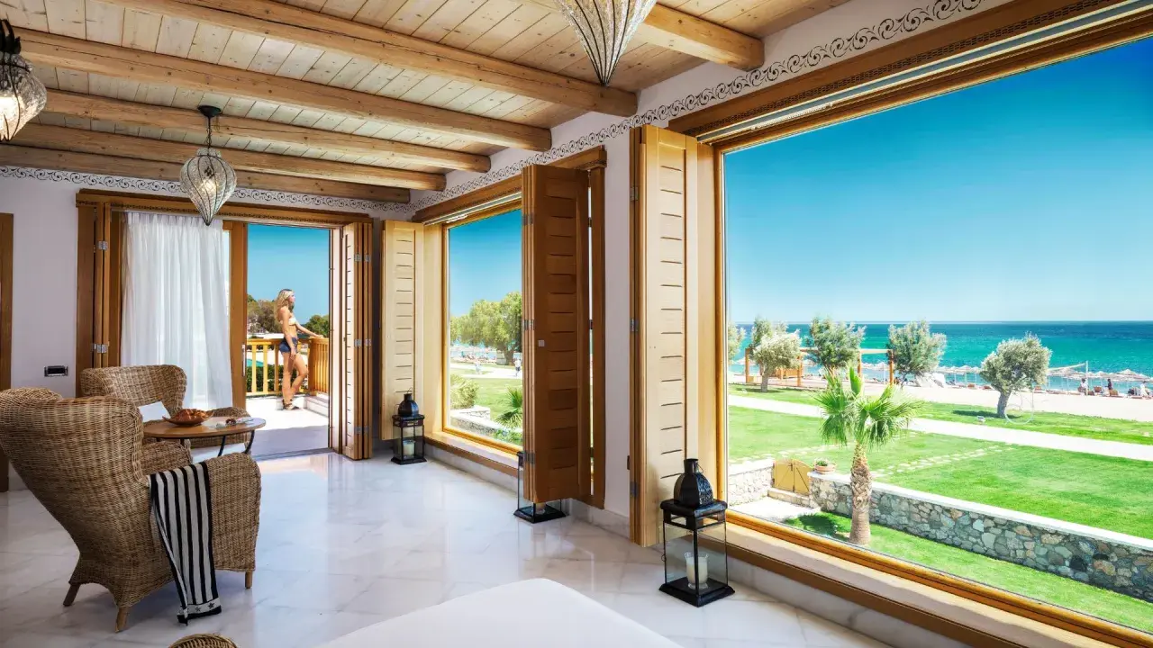 Ein luxuriöses Zimmer mit Meerblick im Mitsis Blue Domes. Eine Frau steht auf dem Balkon und genießt die Aussicht.