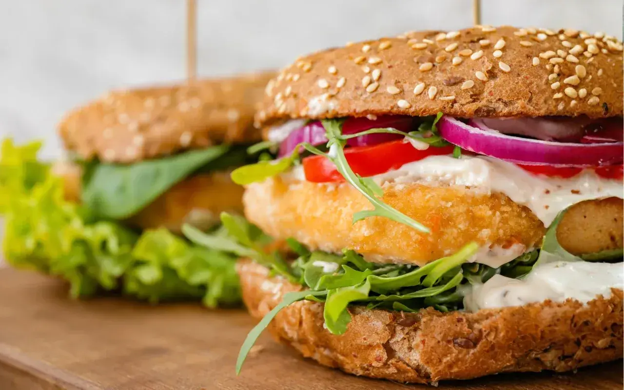 Pyszny burger z krewetkami, chrupiącą sałatą, pomidorem i czerwoną cebulą, polany kremowym sosem.