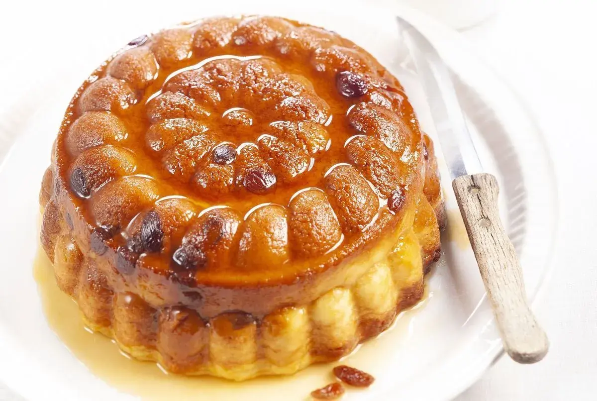 Gâteau de semoule doré et moelleux, nappé d'un sirop ambré et parsemé de raisins secs. Un couteau est posé à côté, prêt à découper cette gourmandise.