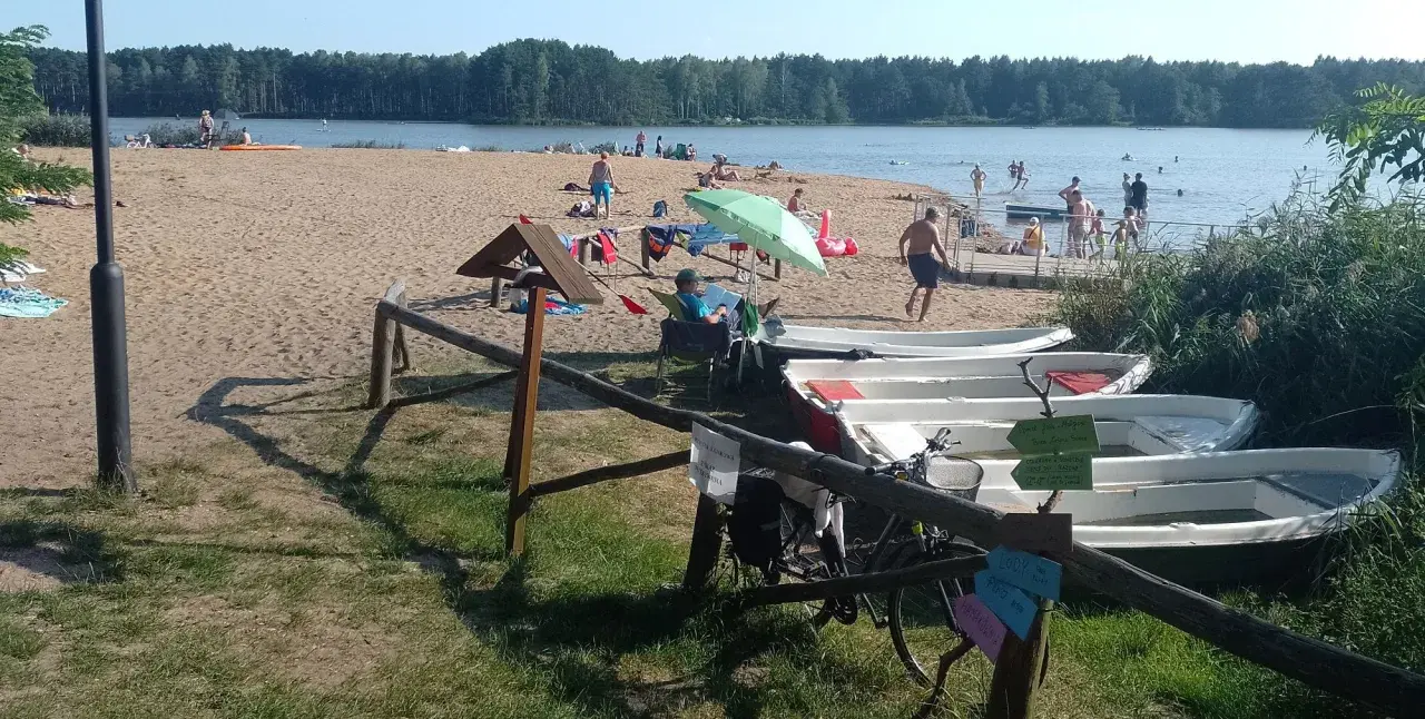 Słoneczny dzień nad zalewem zielona. Ludzie odpoczywają na plaży, kąpią się w wodzie, a obok cumują łódki.