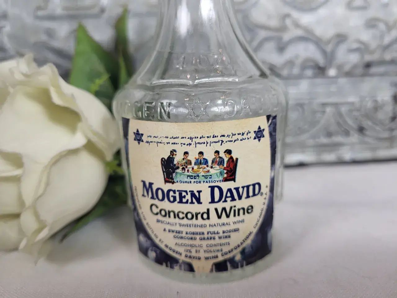 Butelka wina Mogen David Concord Wine z etykietą i białym kwiatem w tle.