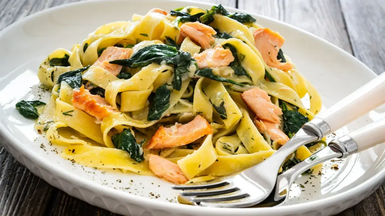 Pappardelle z łososiem i szpinakiem, danie fit, podane na białym talerzu z widelcem i nożem.