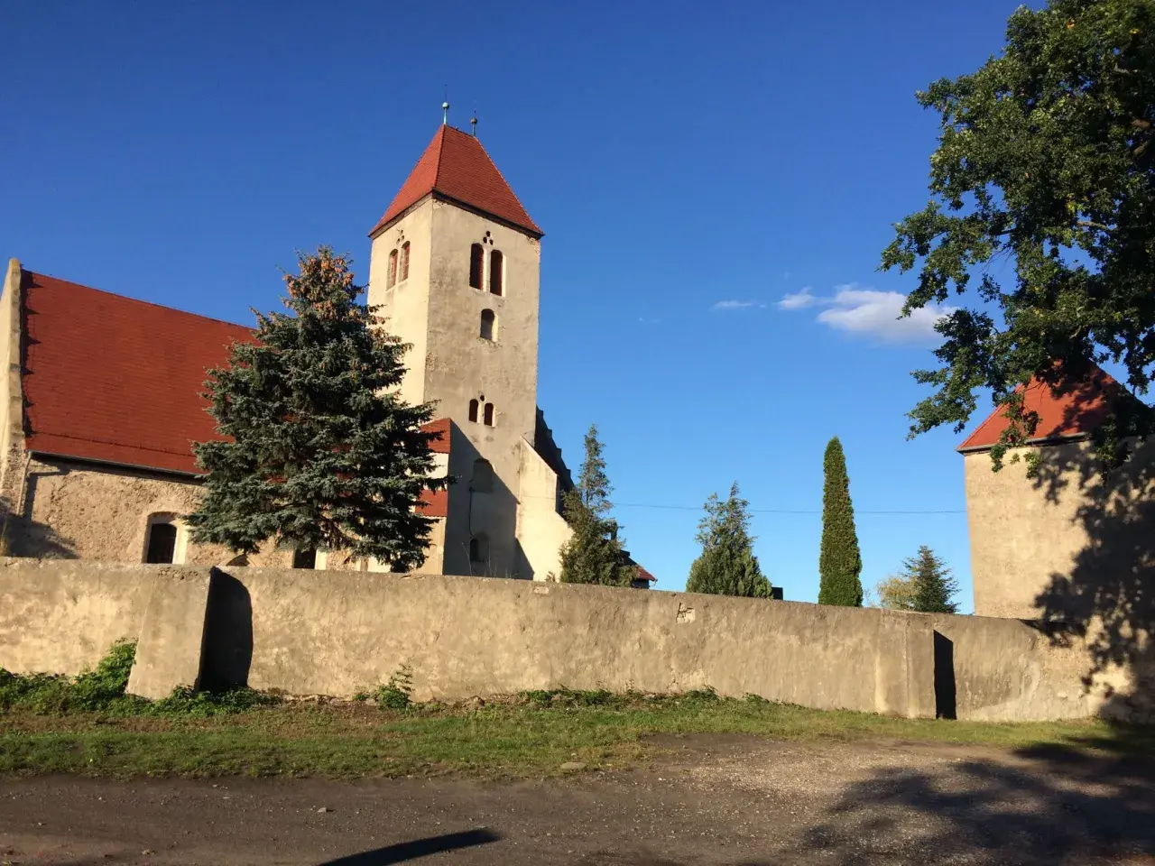 Kamienna wieża kościelna z czerwonym dachem w Nowogród Bobrzański, otoczona murem i zielenią.