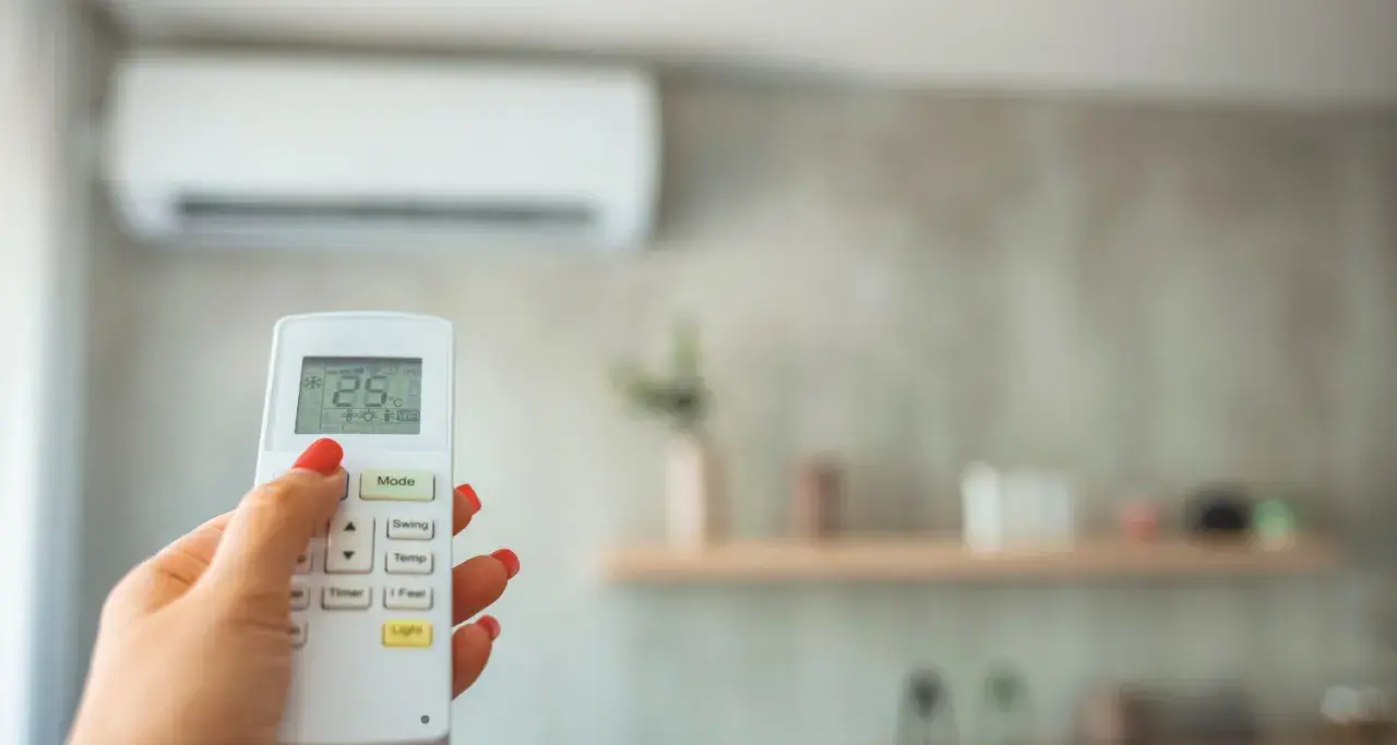 Mano con control remoto para cambiar temperatura aire acondicionado. Pantalla muestra 25°C.