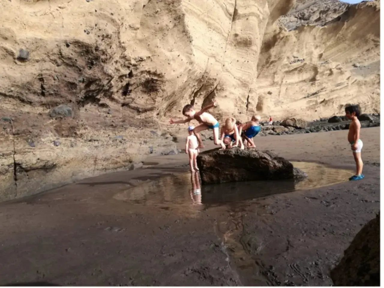 Un grupo de niños exploran una poza en la playa, rodeados de acantilados rocosos.