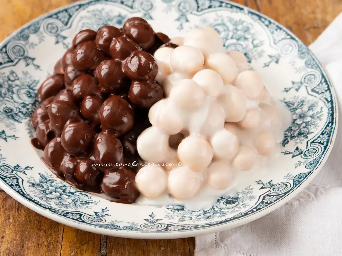 Pignolata messinese: palline dolci ricoperte di cioccolato fondente e glassa bianca, servite su un piatto decorato.