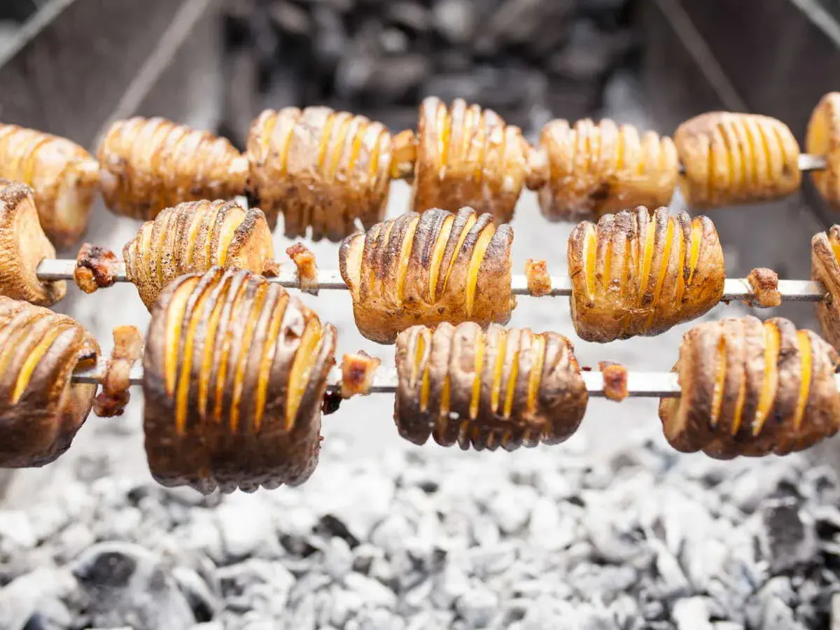 Pommes de terre coupées en accordéon, grillées à la broche sur des braises. Quelle pomme de terre barbecue !