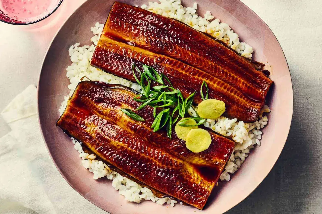 Two glazed unadon fillets rest on a bed of white rice, garnished with green onions and pickled ginger.