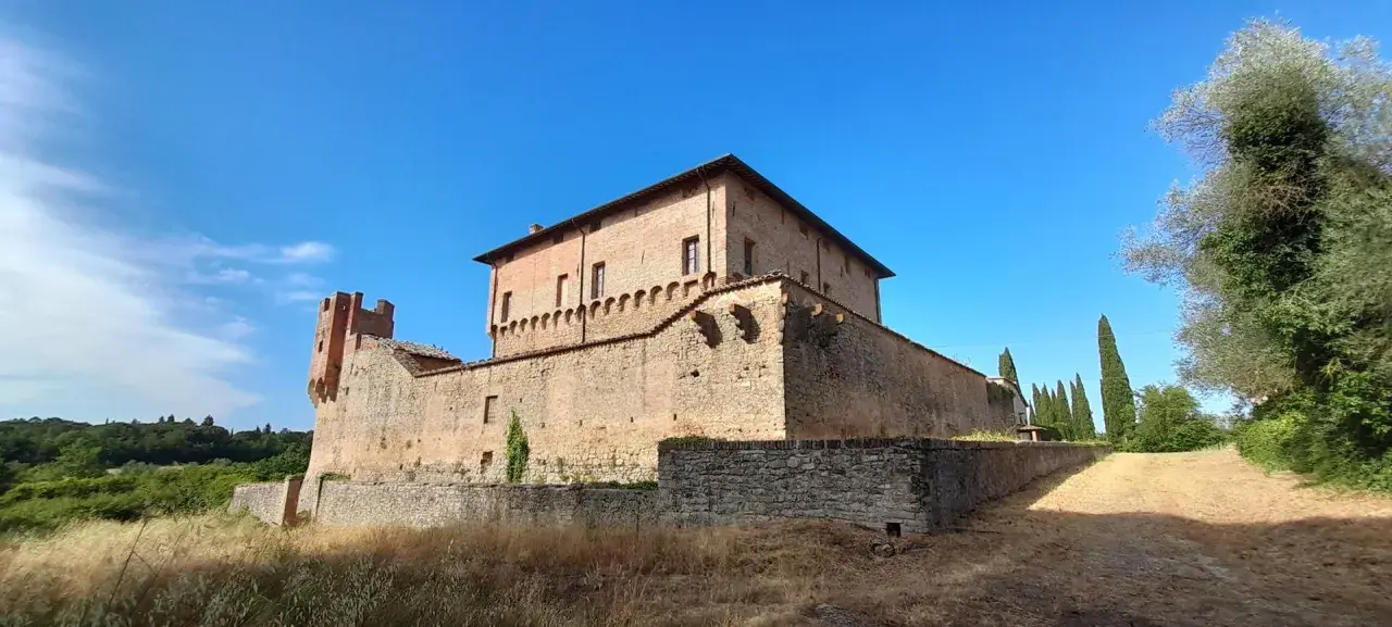 Rocche e mura antiche a Civitella Paganico cosa vedere: un castello medievale in mattoni rossi sotto un cielo azzurro, circondato da vegetazione rigogliosa.