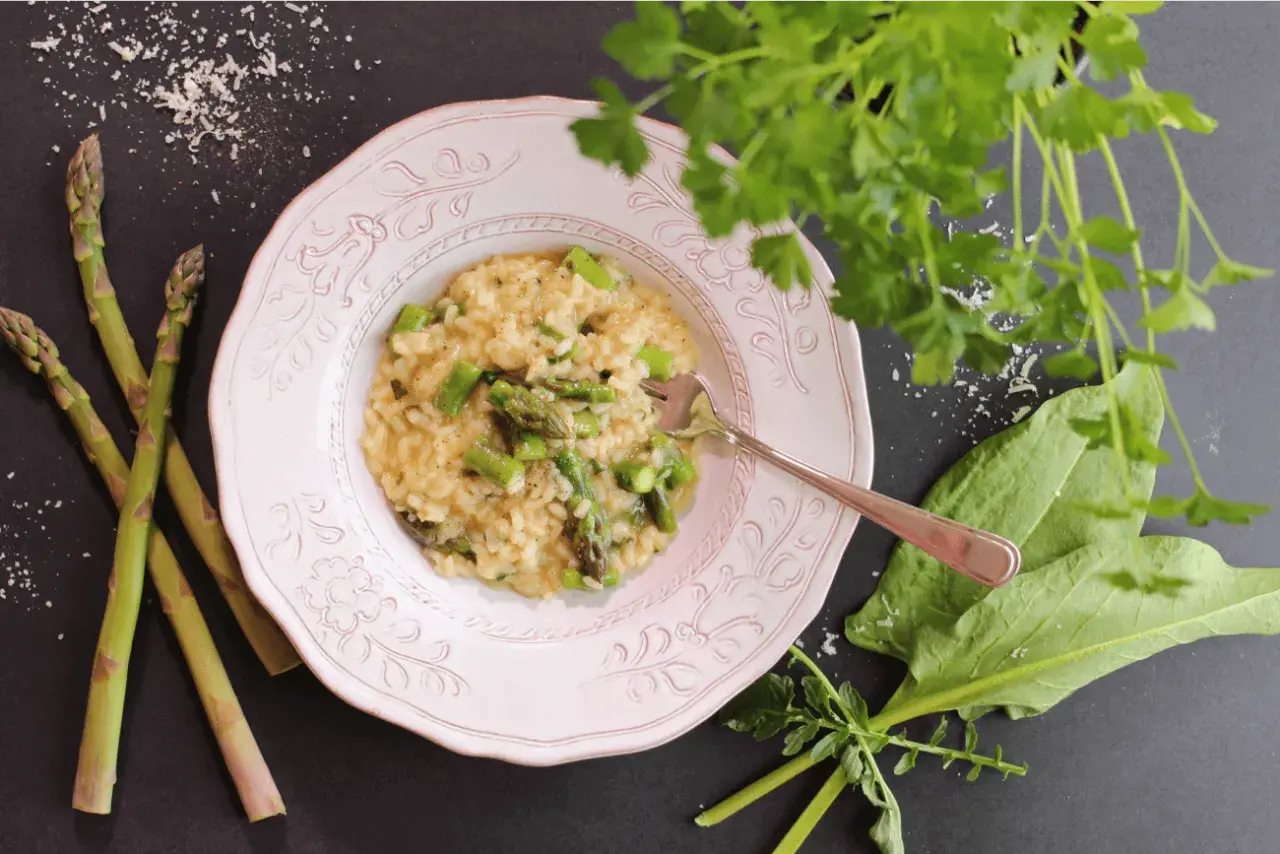 Un crémeux risotto asperges, garni de morceaux d'asperges fraîches, servi dans une assiette rose, avec des asperges crues à côté.
