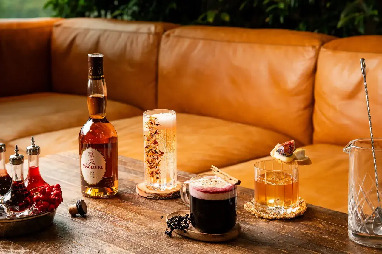 En flaska Calvados står bredvid drinkar och tillbehör på ett träbord.