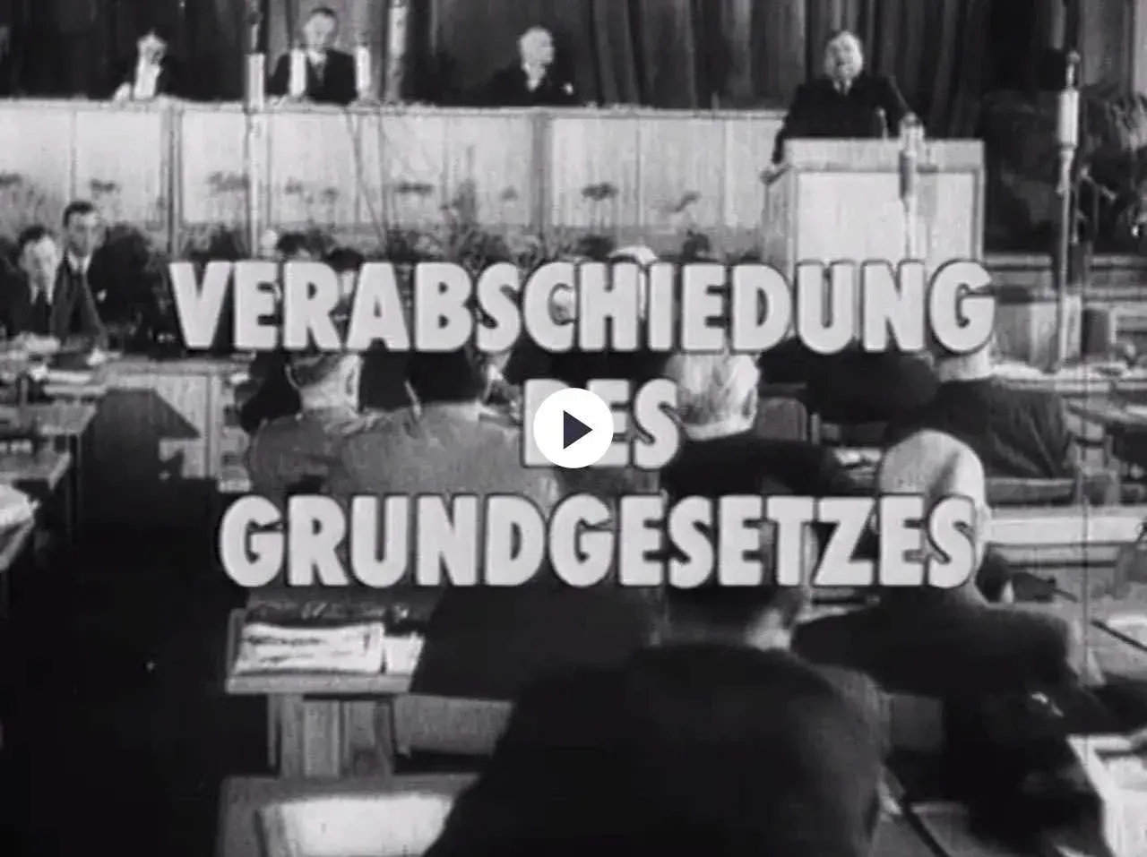 Der parlamentarische Rat verabschiedet das Grundgesetz. Männer in Anzügen sitzen und stehen im Saal.