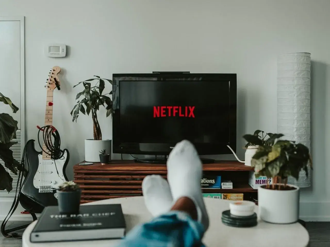 Telewizor z logo Netflix, gitara elektryczna i rośliny w salonie.