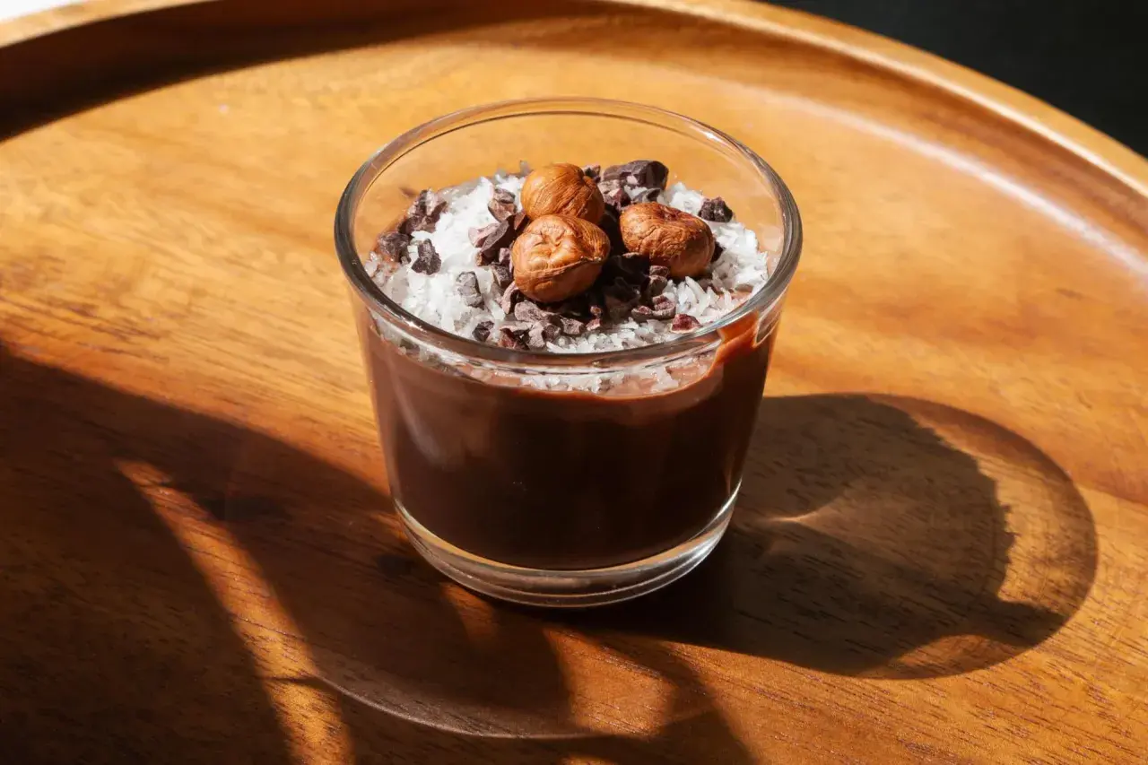 Delizioso dessert in bicchiere con yogurt, cacao, cocco grattugiato e nocciole.