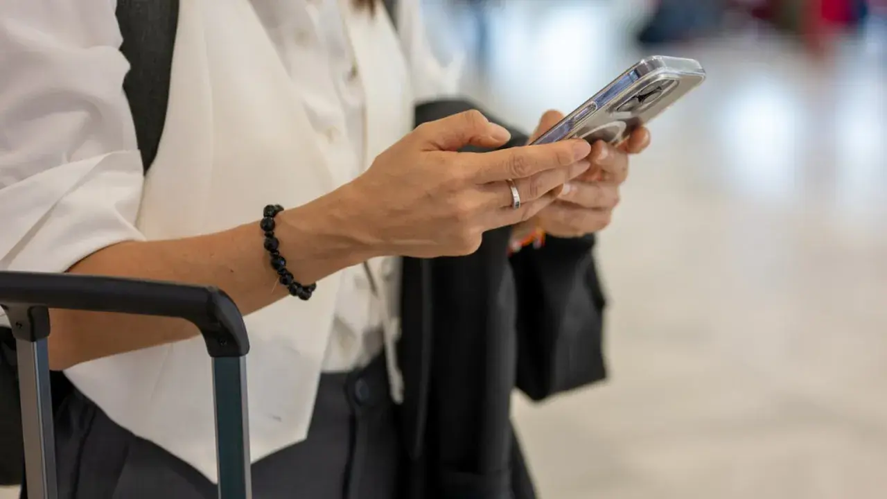 Kobieta z telefonem w dłoni, obok walizki. Sprawdza informacje o wyłączeniu 3G Plus, przygotowując się do podróży.