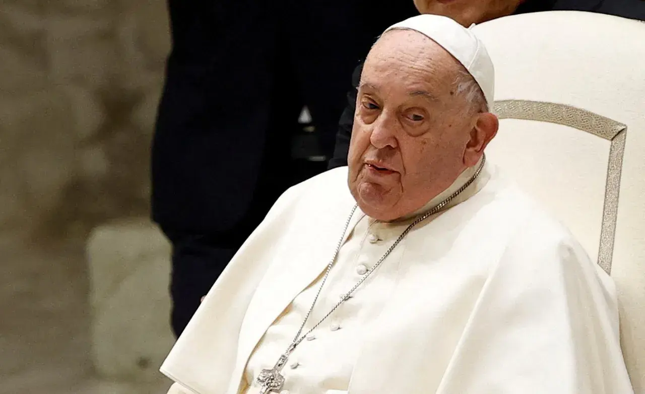Papież Franciszek, siedzący na białym krześle, w białej sutannie i piusce. Jego wzrost jest typowy dla mężczyzny w jego wieku.