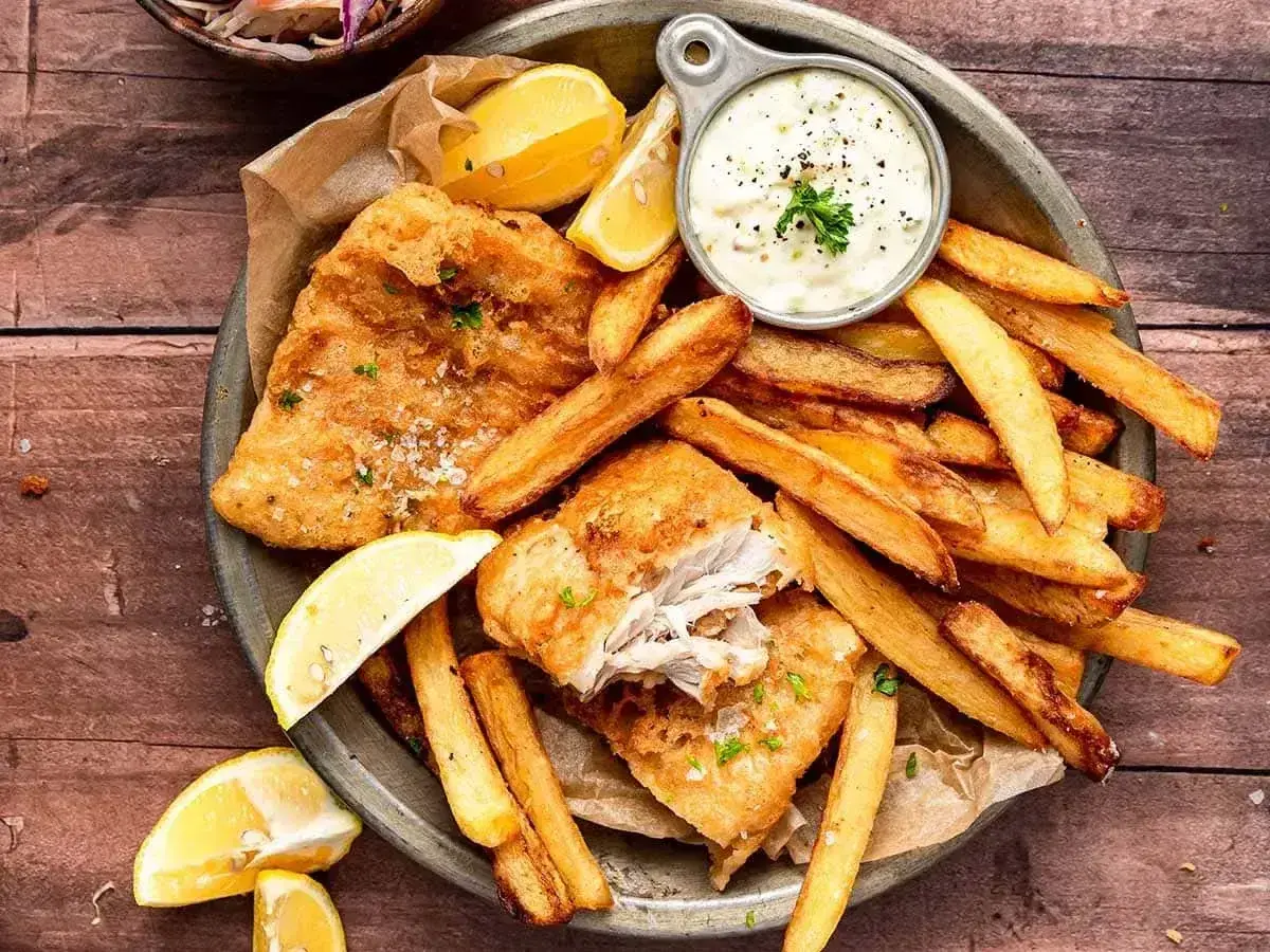 Chrupiące **fish and chips** z cytryną i sosem tatarskim na drewnianym stole. Idealna przekąska!