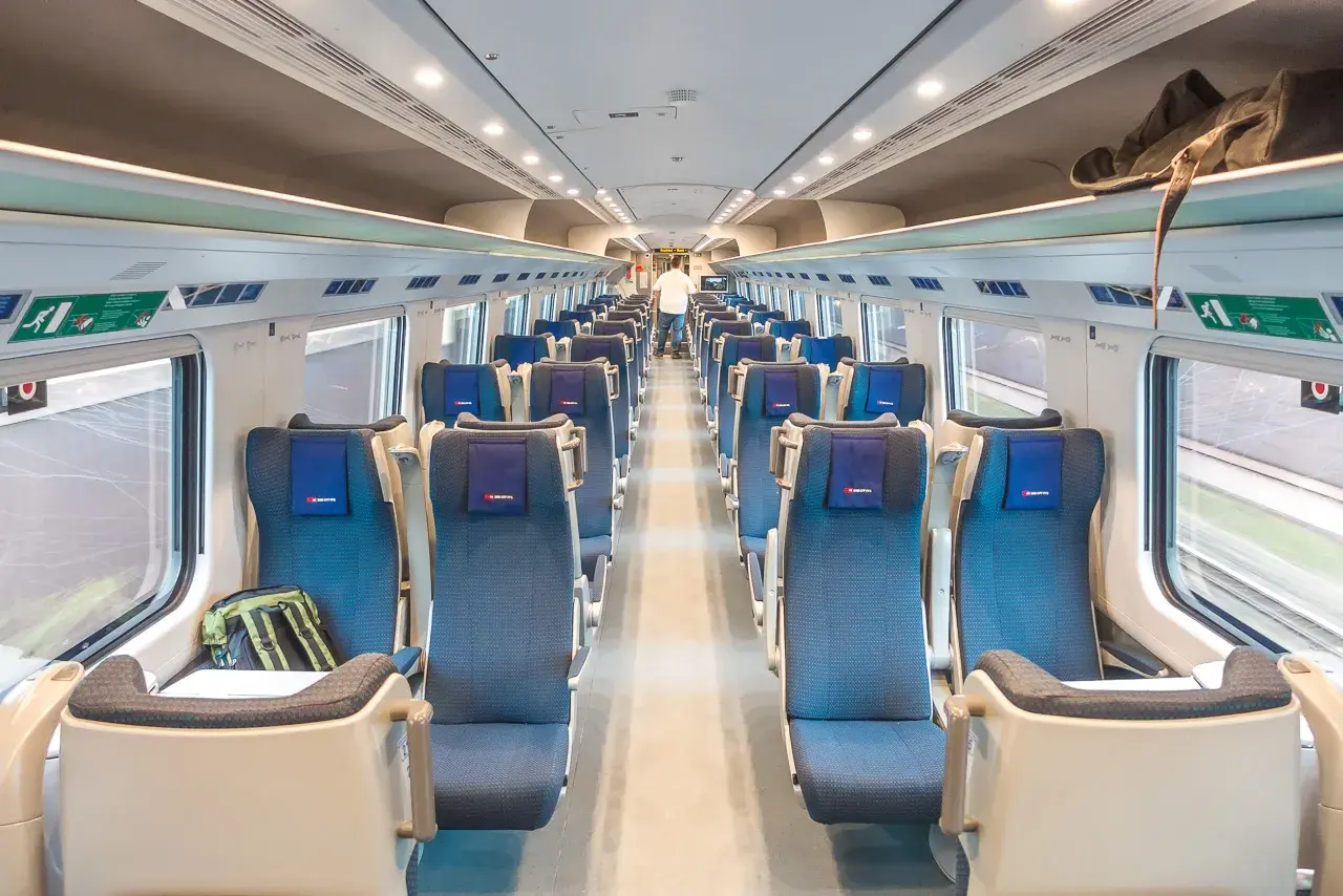 Innenraum eines modernen Euro City Express Zuges mit blauen Sitzen und Gepäckablagen.