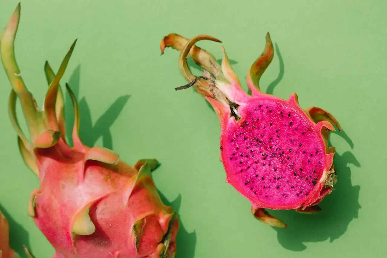 Zwei leuchtend pinke Drachenfrüchte, eine angeschnitten, zeigen ihr gesundes, kernreiches Inneres auf grünem Hintergrund.