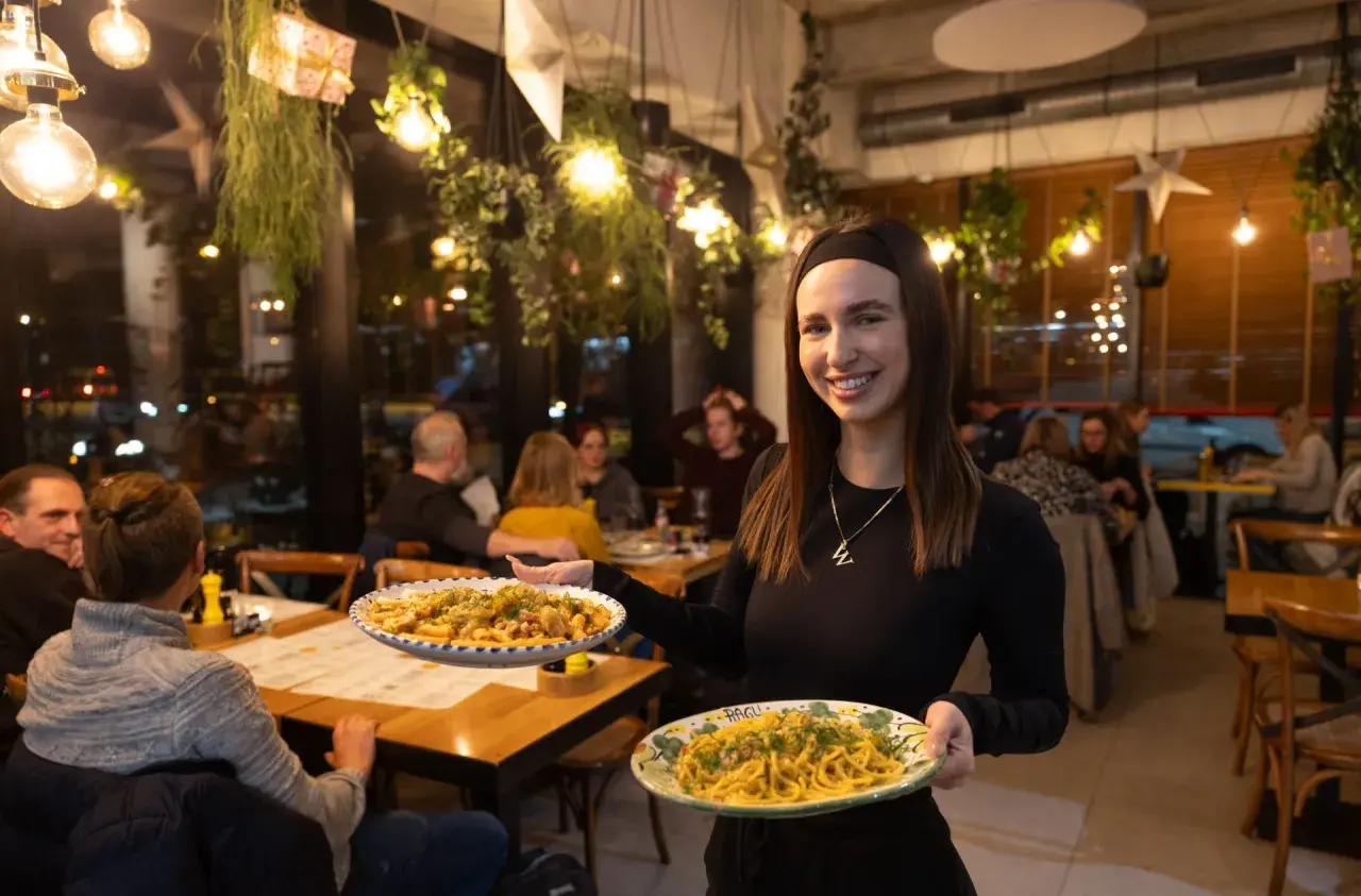 Uśmiechnięta kelnerka serwuje pyszne dania w najlepszej włoskiej restauracji we Wrocławiu. Aromatyczne makarony kuszą z talerzy.