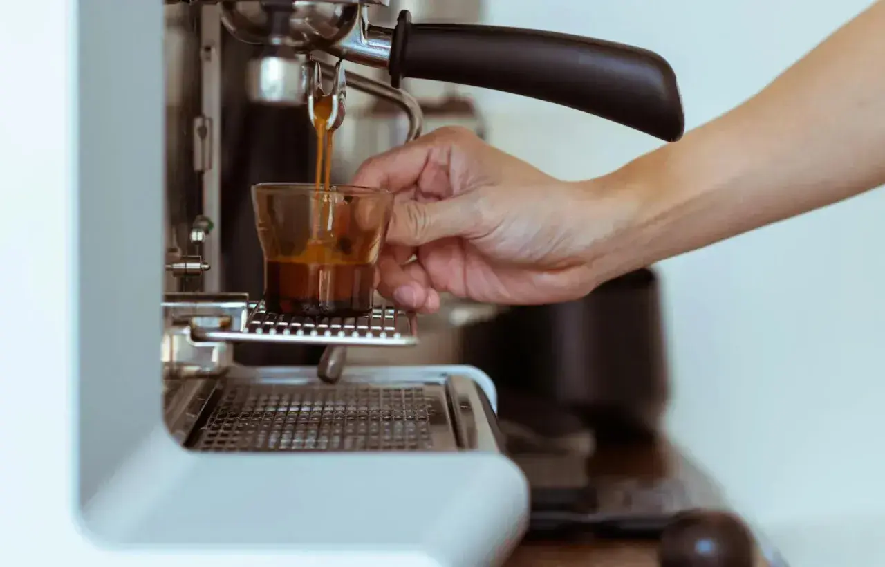 Eine Hand hält ein Glas, während frisch gebrühter Espresso manuell zubereitet wird.