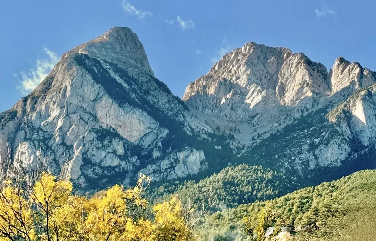 Majestuosas montañas de el Pedraforca bajo un cielo azul. El sol ilumina las cumbres rocosas y los bosques verdes.