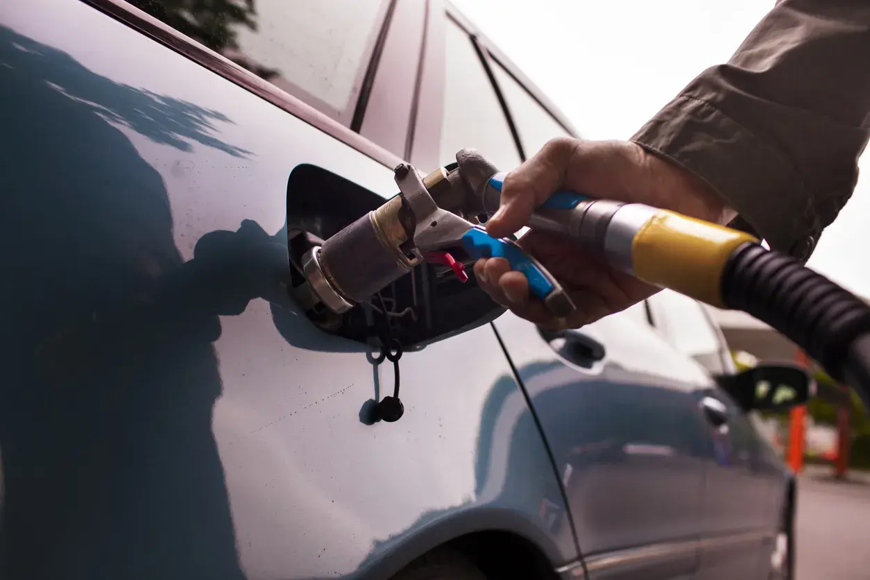 Rifornimento GPL. Se la bombola gpl scaduta posso circolare a benzina? La mano inserisce la pistola di rifornimento nel serbatoio dell'auto.