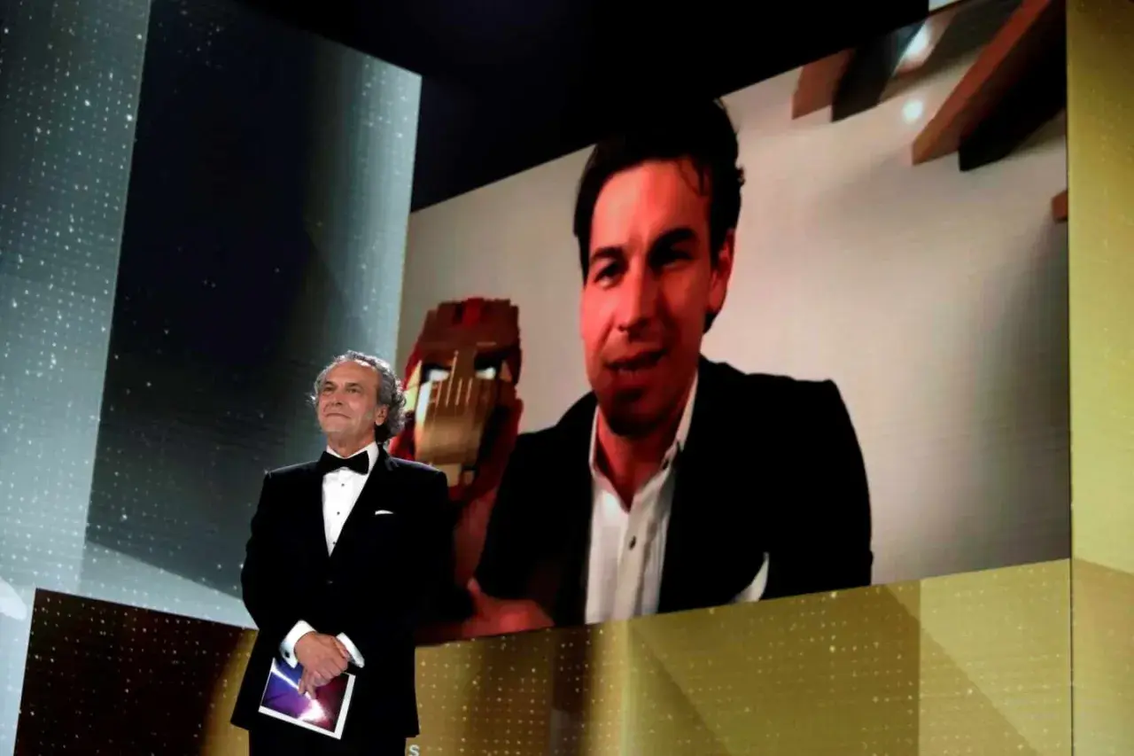 Presentador en los Goya con Mario Casas en pantalla, quien sostiene un premio.