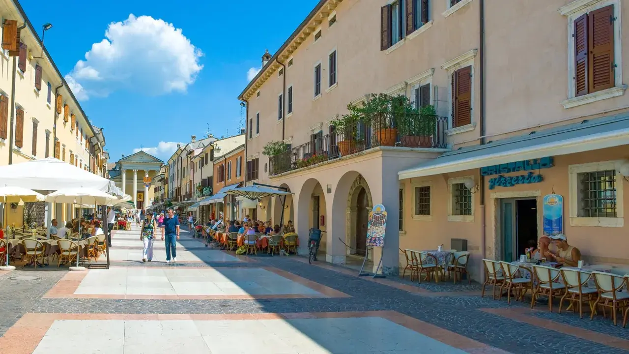 Passeggiata nel bardolino centro storico, con tavolini all'aperto e gente che gode del sole.