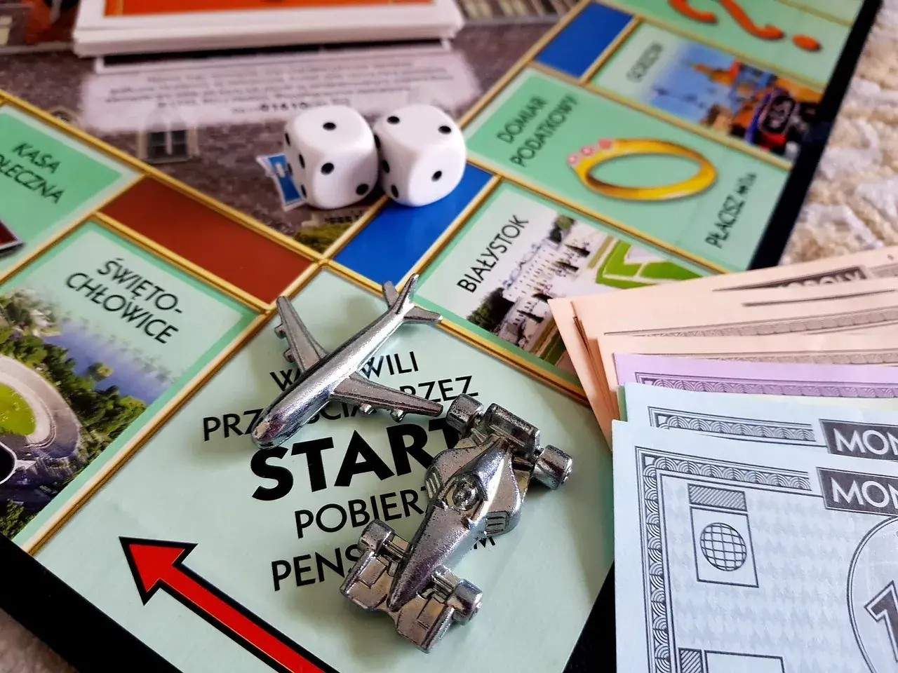 Plansza Monopoly z pionkami (samolot, bolid), kostkami i banknotami.