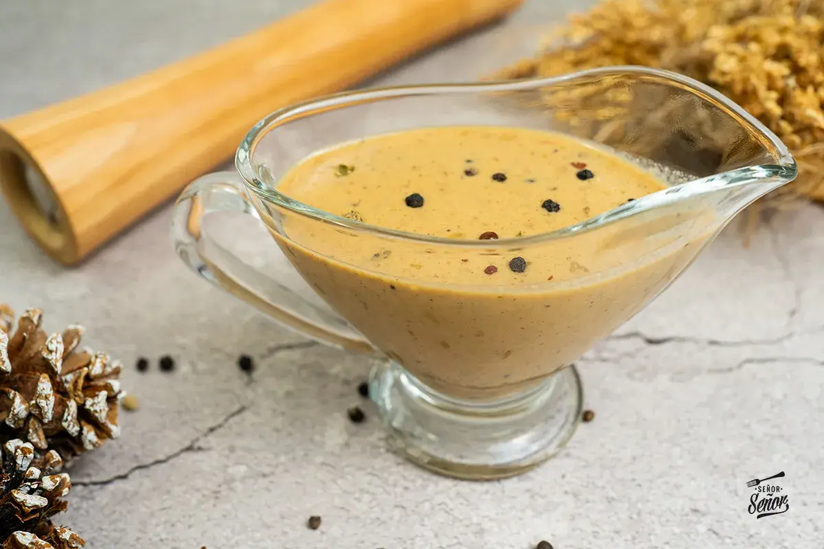 Salsa a la pimienta cremosa en una salsera de cristal, con granos de pimienta negra esparcidos.
