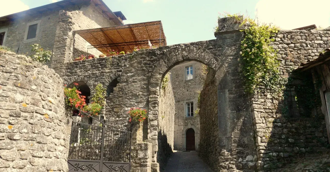 Un vicolo suggestivo a Casola in Lunigiana, con un arco in pietra, fiori rossi e edera rampicante.