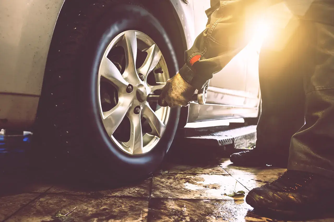 Mechanik w rękawicy używa klucza do odkręcenia koła samochodu. Pokazane jest, jak odkrecic kolo.
