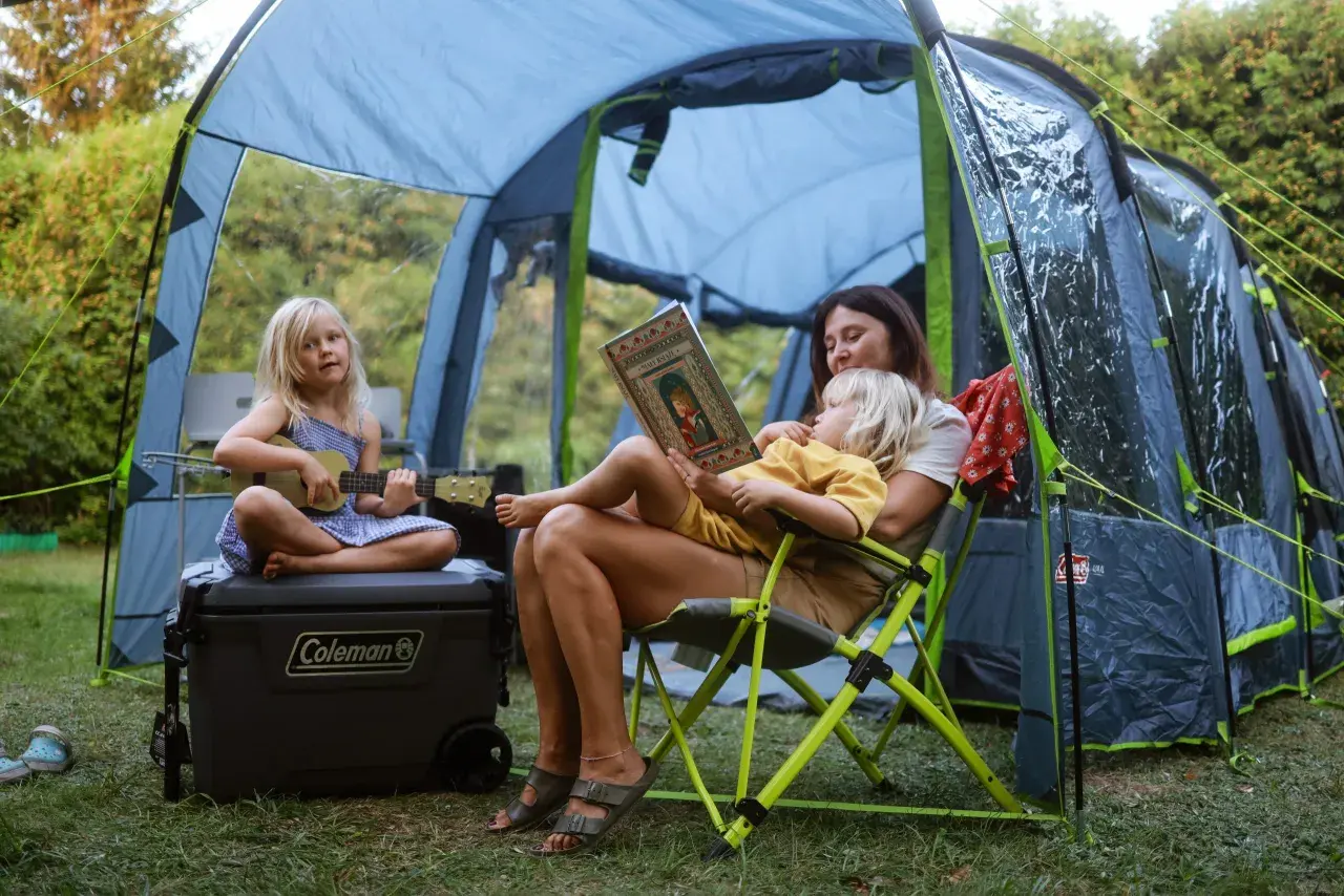 Mama czyta dzieciom w namiocie w Polsce. Jedno dziecko gra na ukulele, drugie słucha bajki. Idealne miejsce, gdzie pod namiot z dziećmi w Polsce.
