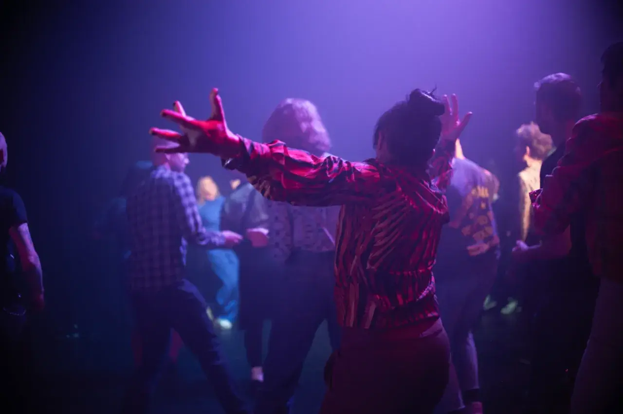 Publiken njuter av en konsert på kulturhuset. En kvinna i röd mönstrad tröja dansar med armarna uppsträckta.