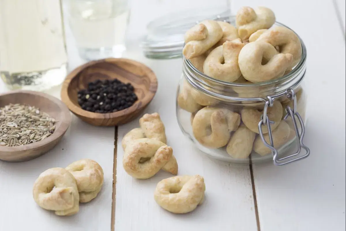 Taralli que es: crujientes bocaditos horneados, algunos en un frasco, con granos de pimienta y hinojo cerca.