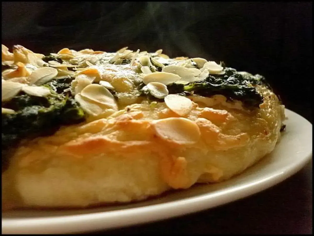 Eine köstliche Spinat Pizza mit knusprigem Teig und gerösteten Mandelblättchen. Dampf steigt auf und verspricht ein warmes, herzhaftes Gericht.