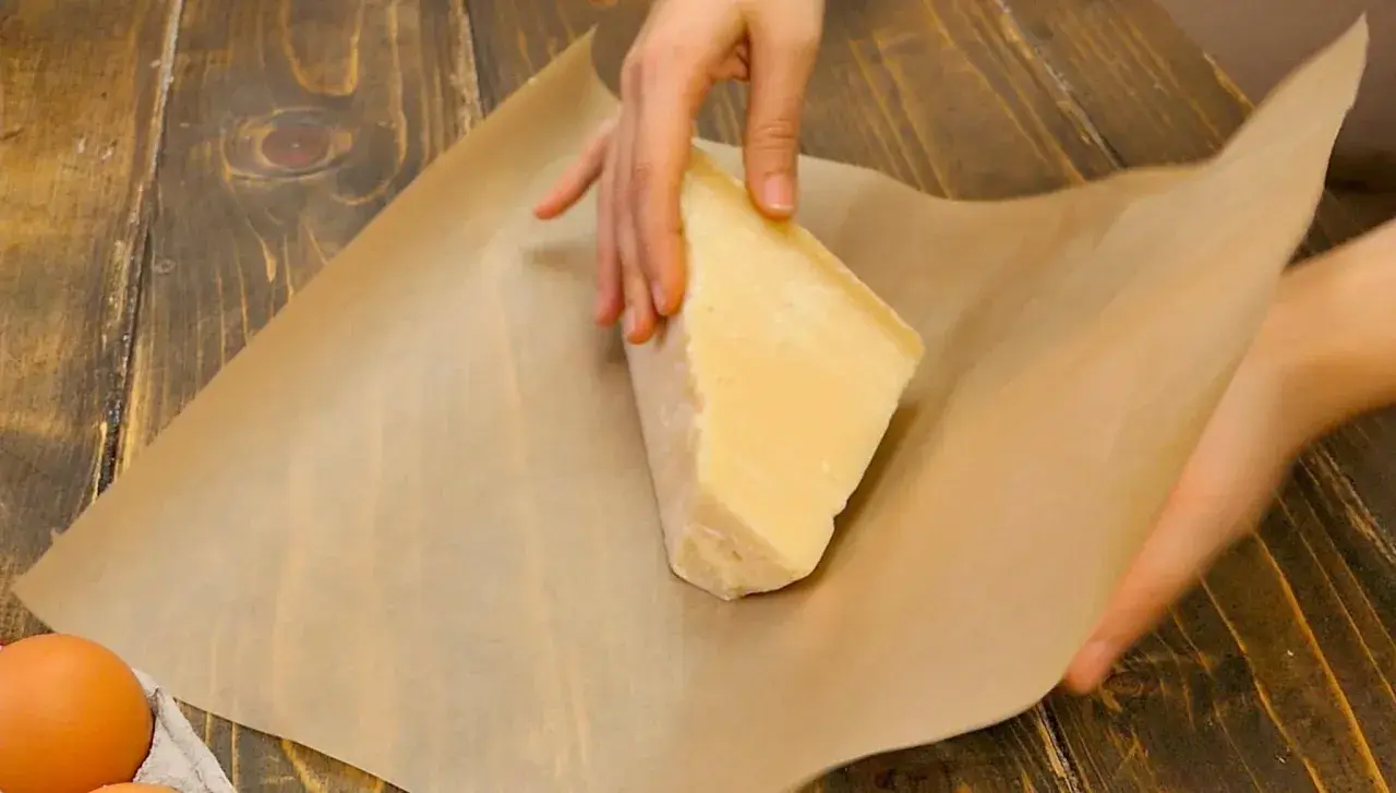 Mani che avvolgono un pezzo di formaggio stagionato nella carta forno, un metodo per conservare il formaggio al meglio.