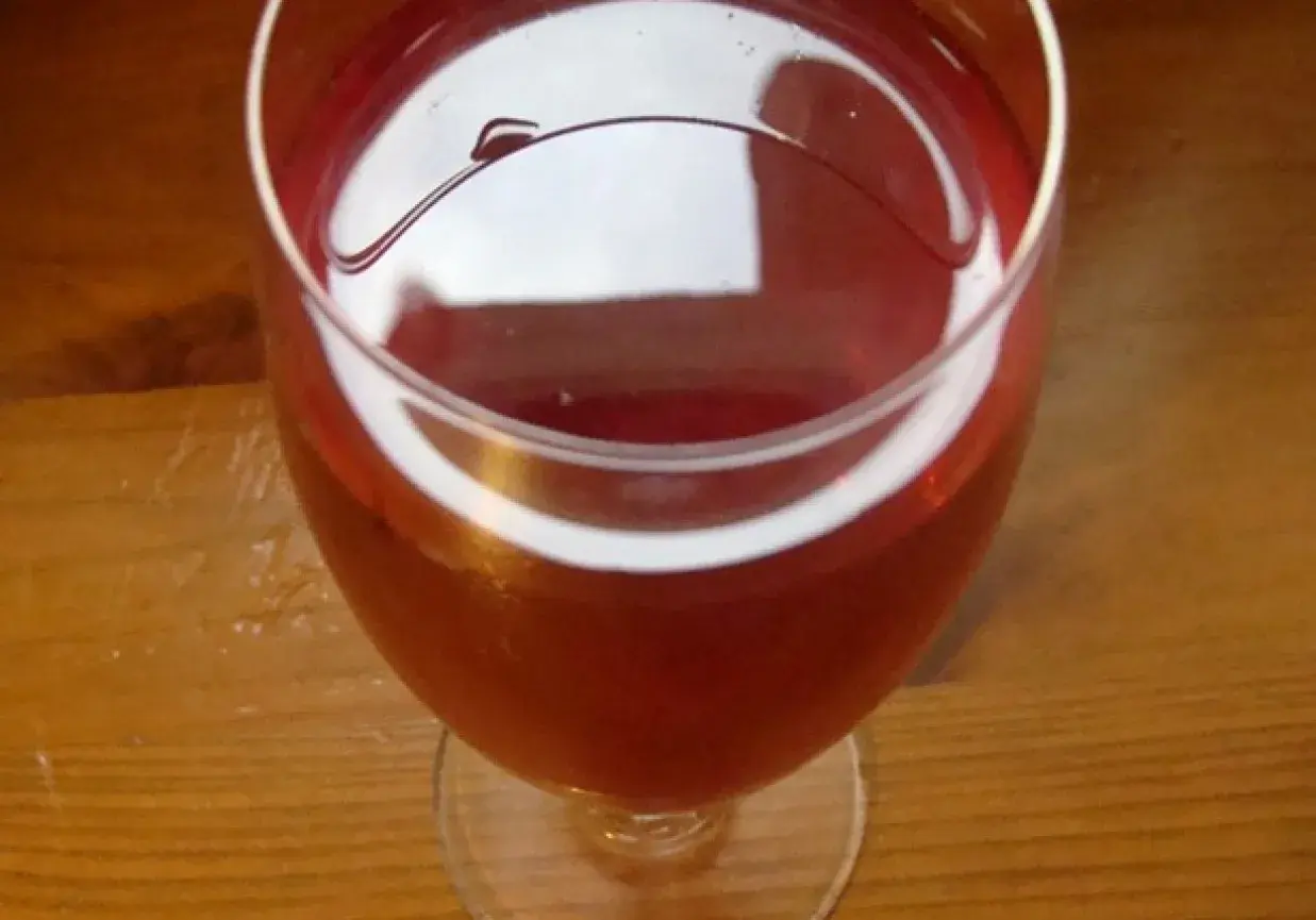 Czerwone wino z róży w kieliszku, na drewnianym stole. Delikatny, rubinowy kolor napoju.