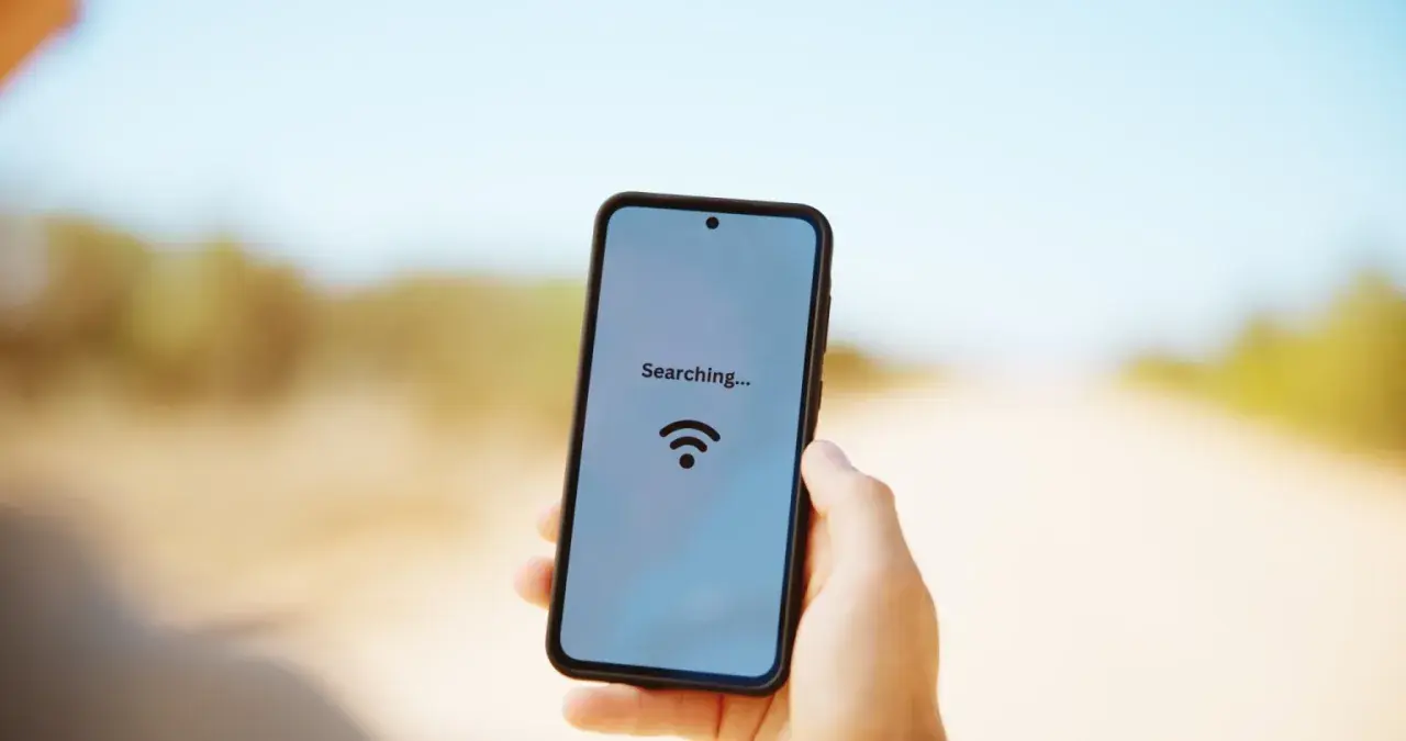 Dłoń trzyma smartfon z napisem "Searching..." i ikoną Wi-Fi na tle drogi.