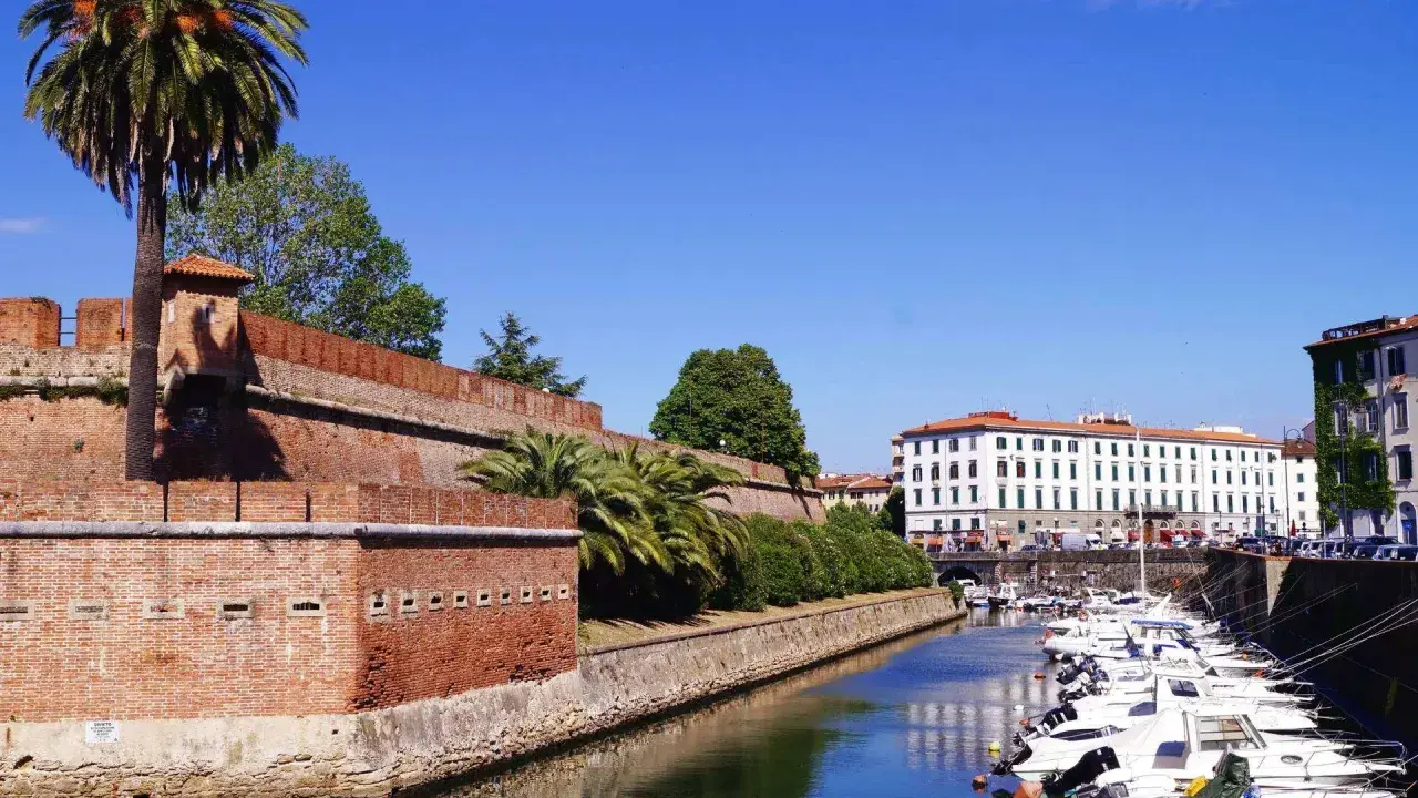 Canal bordé de bateaux à Livourne, Italie, avec une ancienne muraille de briques et des palmiers.