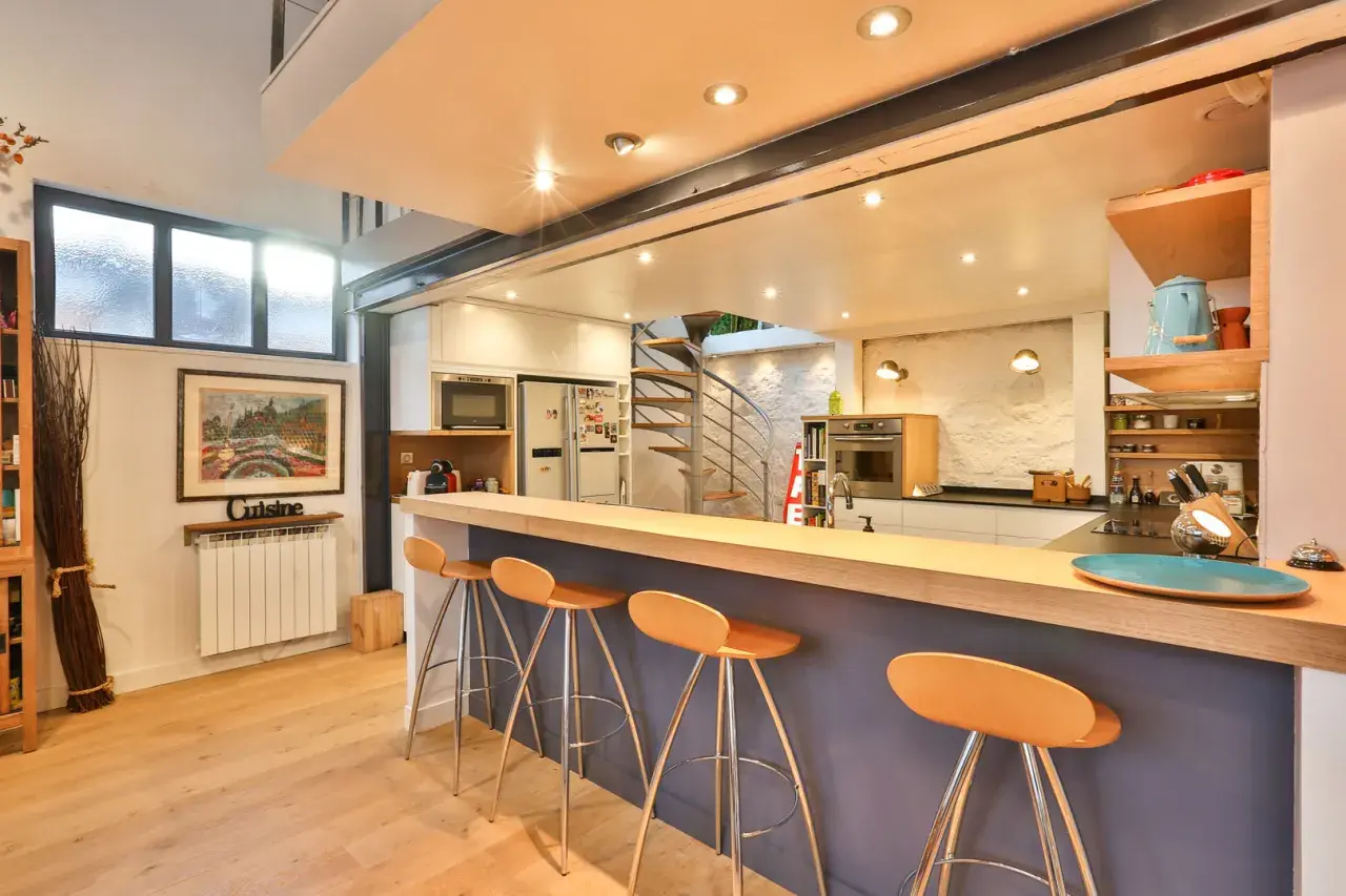 Un bar fait maison original avec des tabourets orange vif, une cuisine moderne et un escalier en colimaçon.