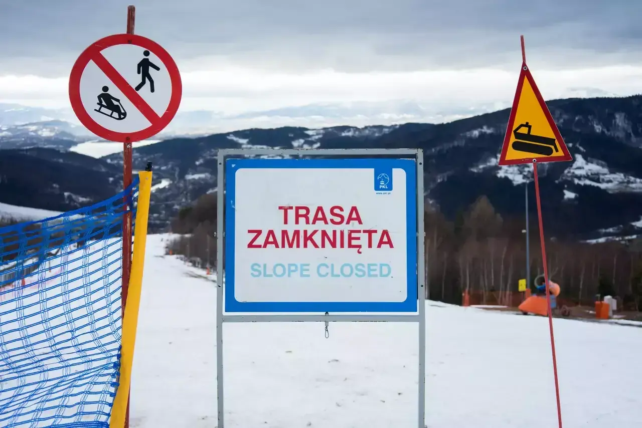 Na stoku narciarskim widoczne są wskaźniki kolejowe: zakaz saneczkarstwa, tablica "Trasa zamknięta" oraz znak ostrzegawczy z ratrakiem.