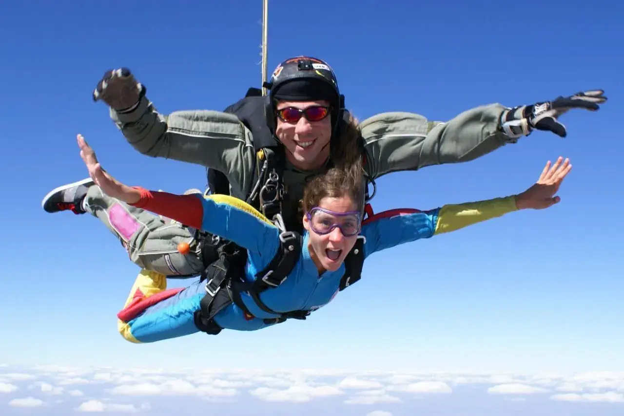 Deux personnes en tandem profitent de la vitesse d'un saut en parachute, bras écartés, au-dessus des nuages.