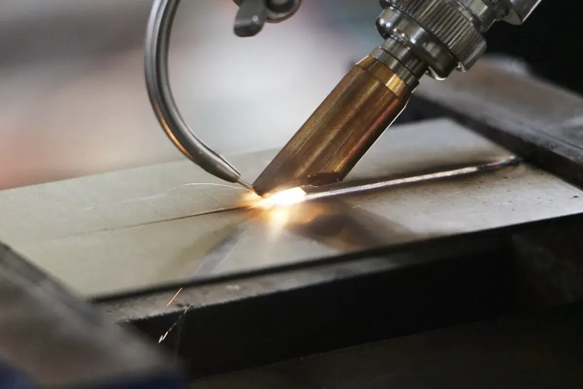 Precyzyjne spawanie laserowe aluminium, tworzące idealne połączenie dwóch elementów. Iskry i jasny łuk świadczą o wysokiej temperaturze procesu.