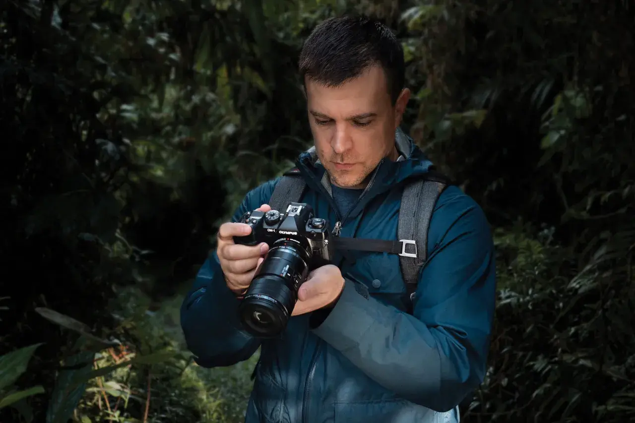 Mężczyzna w lesie trzyma aparat OM-1 Olympus, przygotowując się do makrofotografii sprzętu.