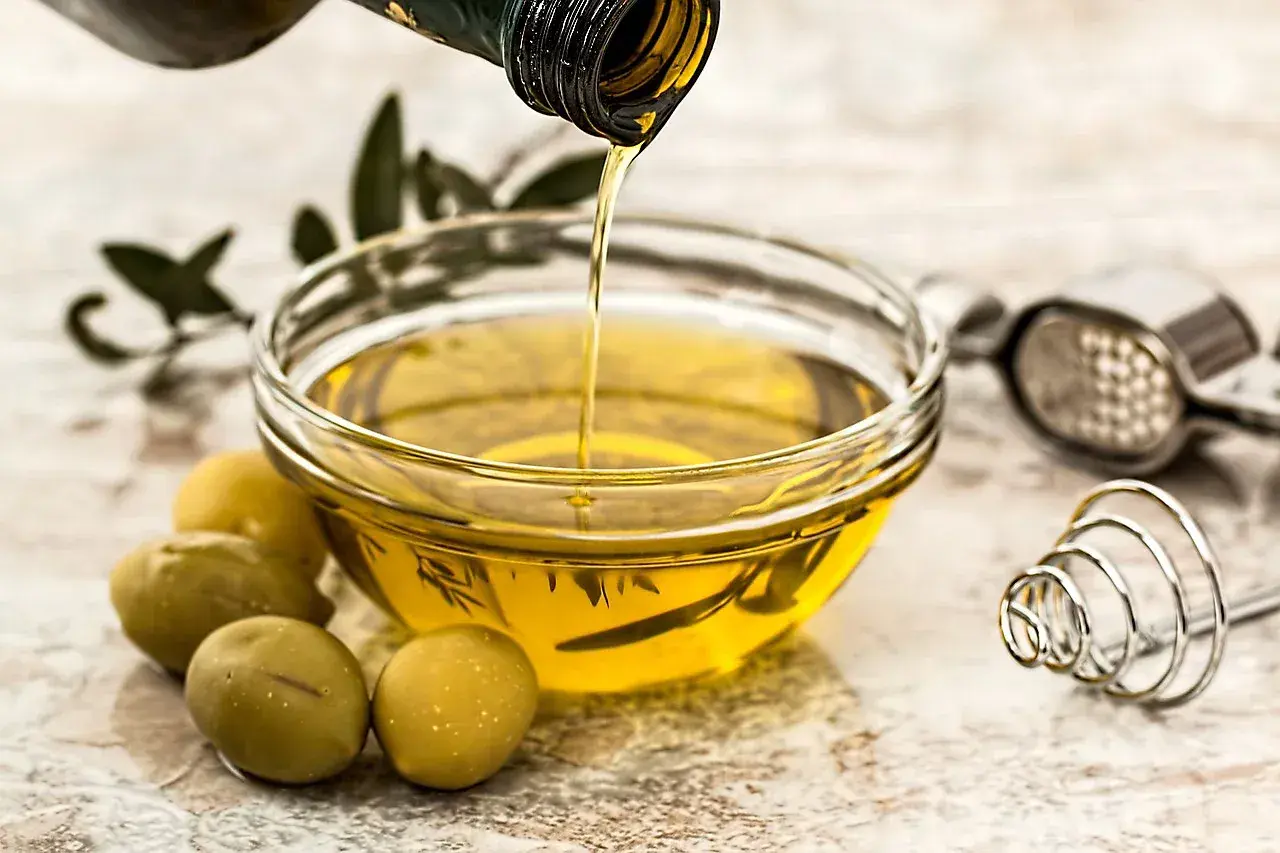 Olio d'oliva versato in una ciotola, pronto per friggere. Olive verdi e un pestello completano la scena.