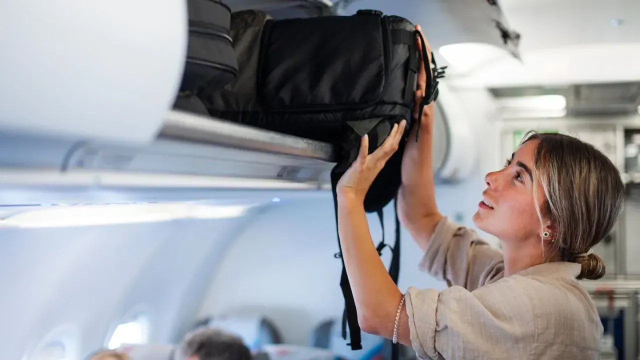 Junge Frau verstaut ihren großen Backpacking Rucksack im Gepäckfach eines Flugzeugs.