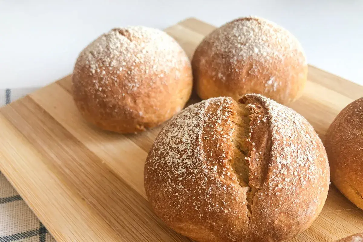 Pane dorato e fragrante, appena sfornato nella friggitrice ad aria, cosparso di farina su un tagliere di legno.