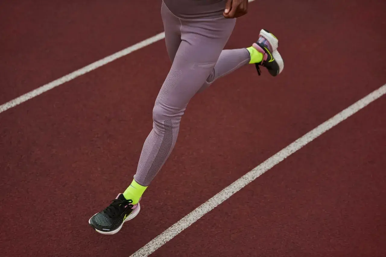 Une athlète court sur une piste, portant une chaussure de marche longue distance et des chaussettes fluo.